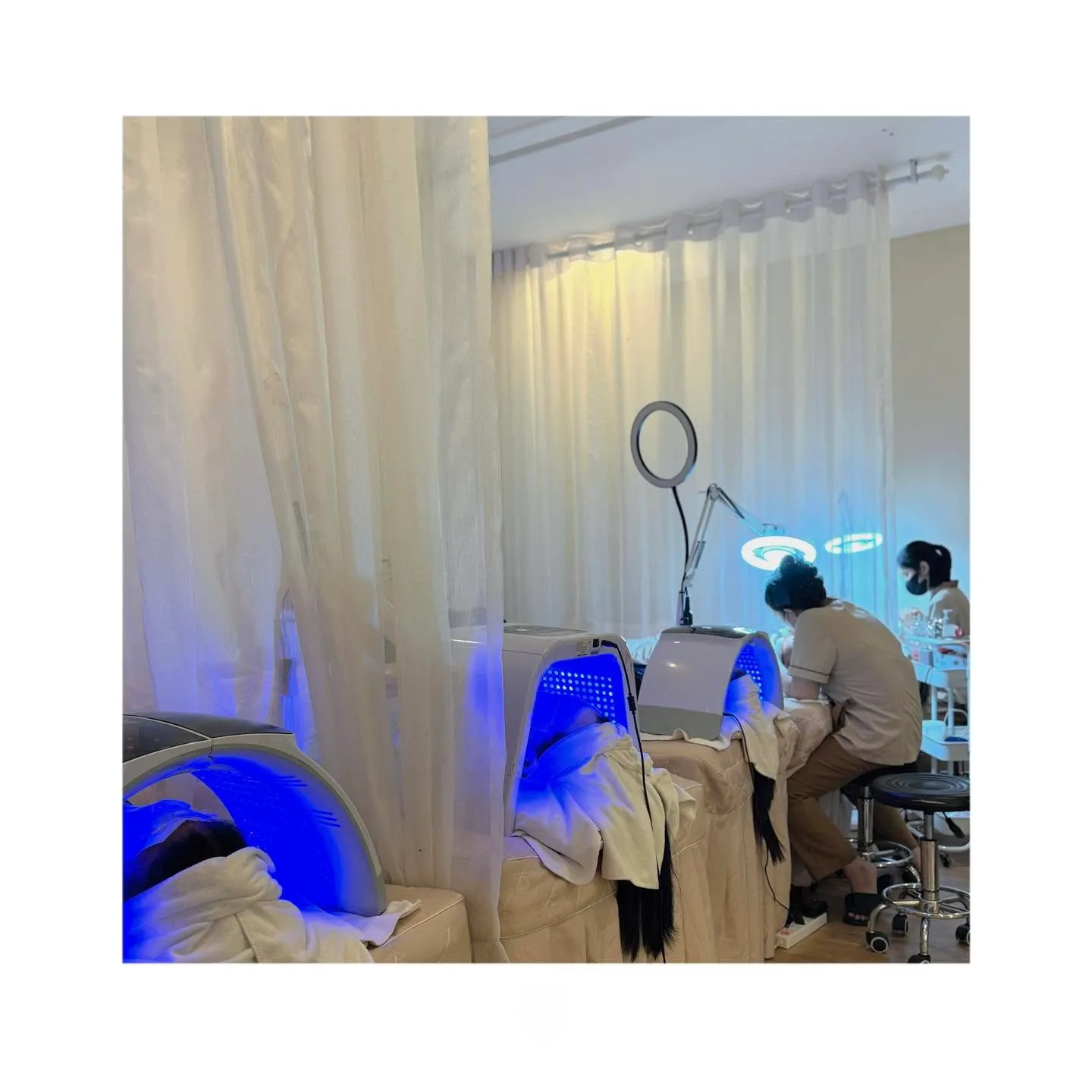 Khách nằm dưới máy đèn LED xanh sau rèm trắng, kỹ thuật viên làm việc bên cạnh