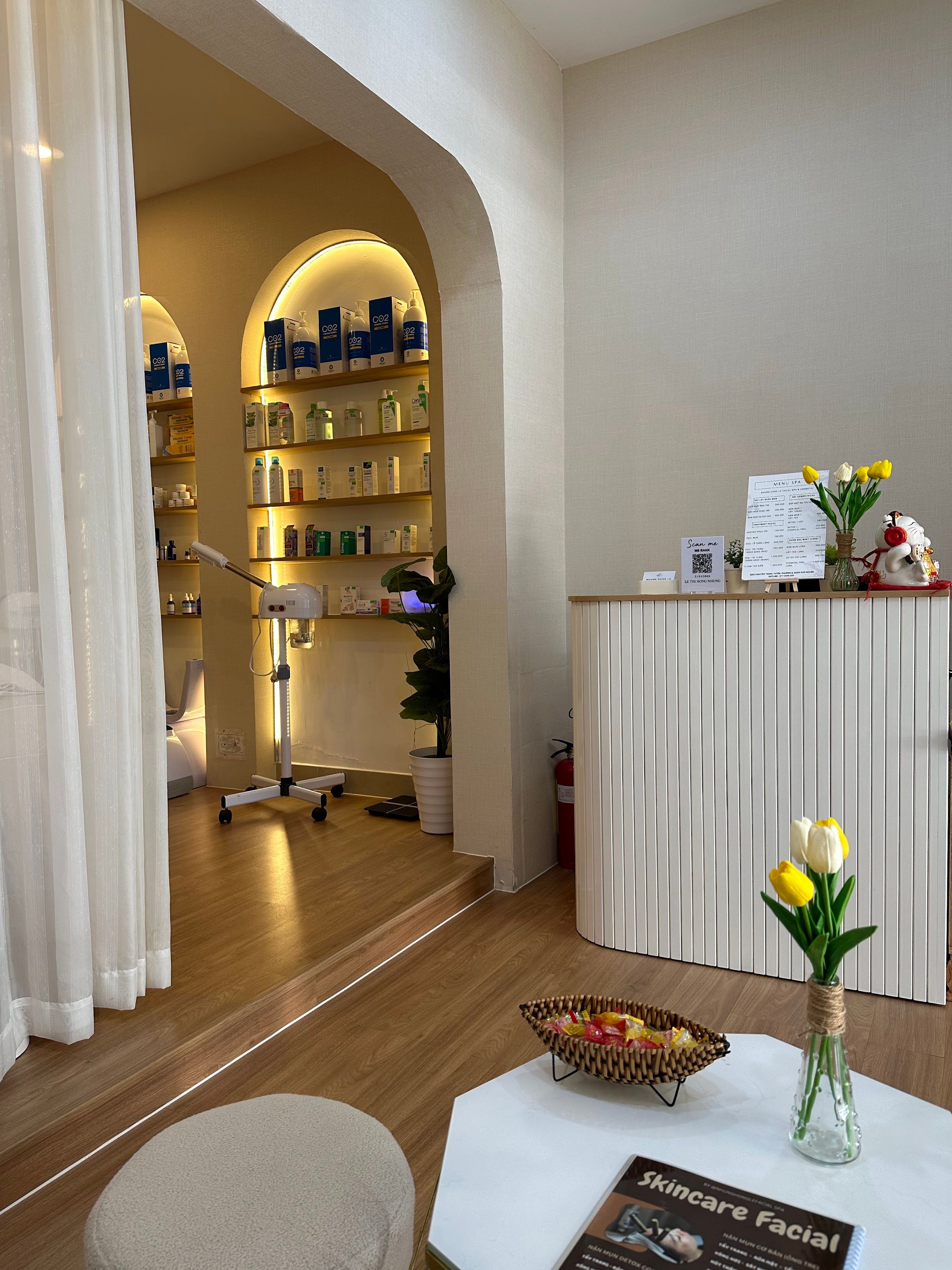 Quầy tiếp đón có hoa tulip, phía sau là vòm kệ dược mỹ phẩm và máy xông hơi của spa