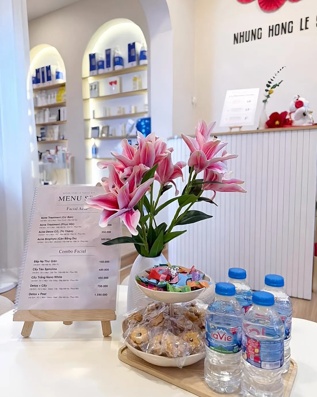 Quầy đón khách sáng với bình hoa ly hồng và kệ dược mỹ phẩm